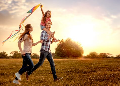 Happy Family Running Through A Field With A Kite To Represent Reflecting As A Fostering Agency