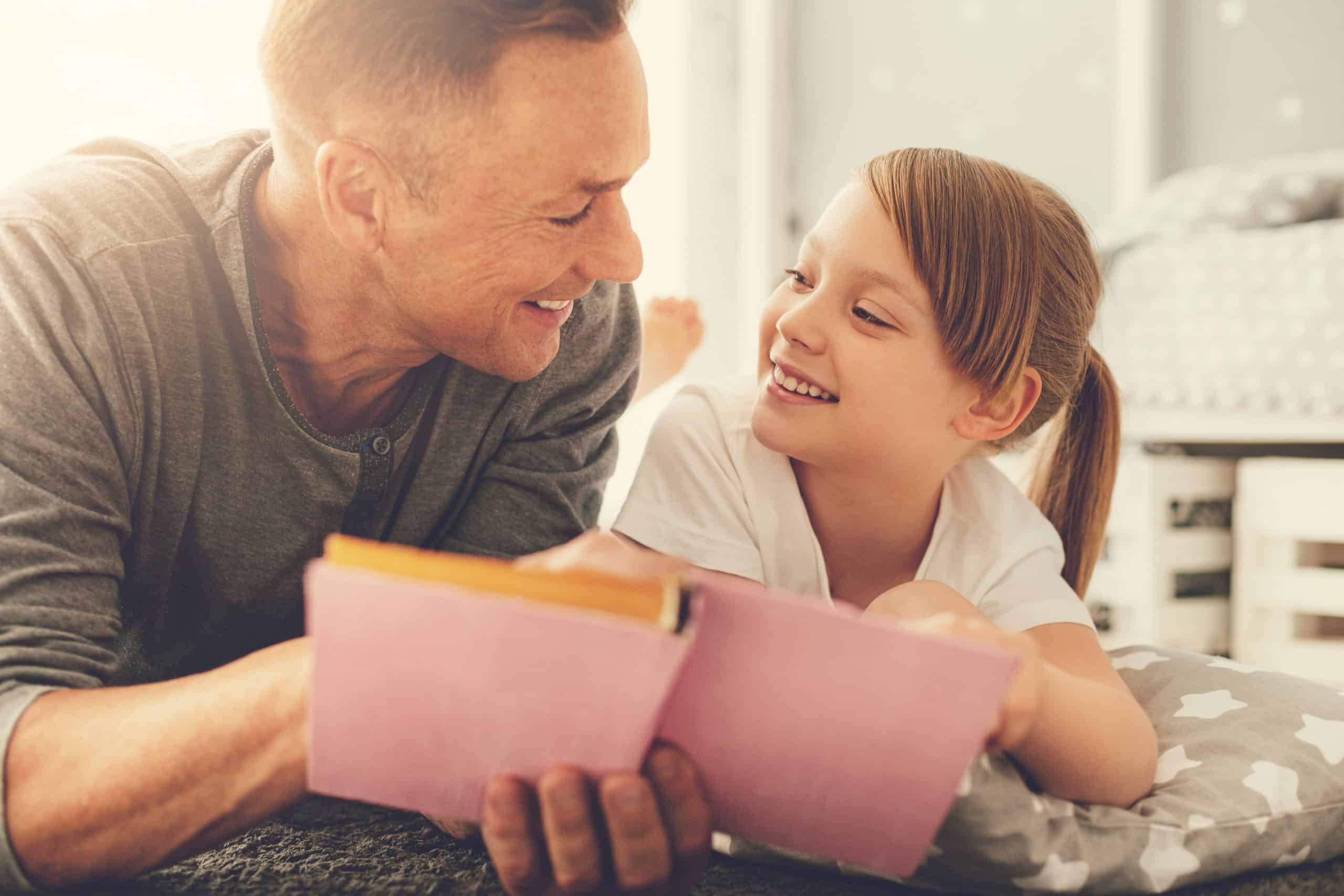 Father and Daughter Lying On Bed Reading Story to Represent Therapeutic Parent